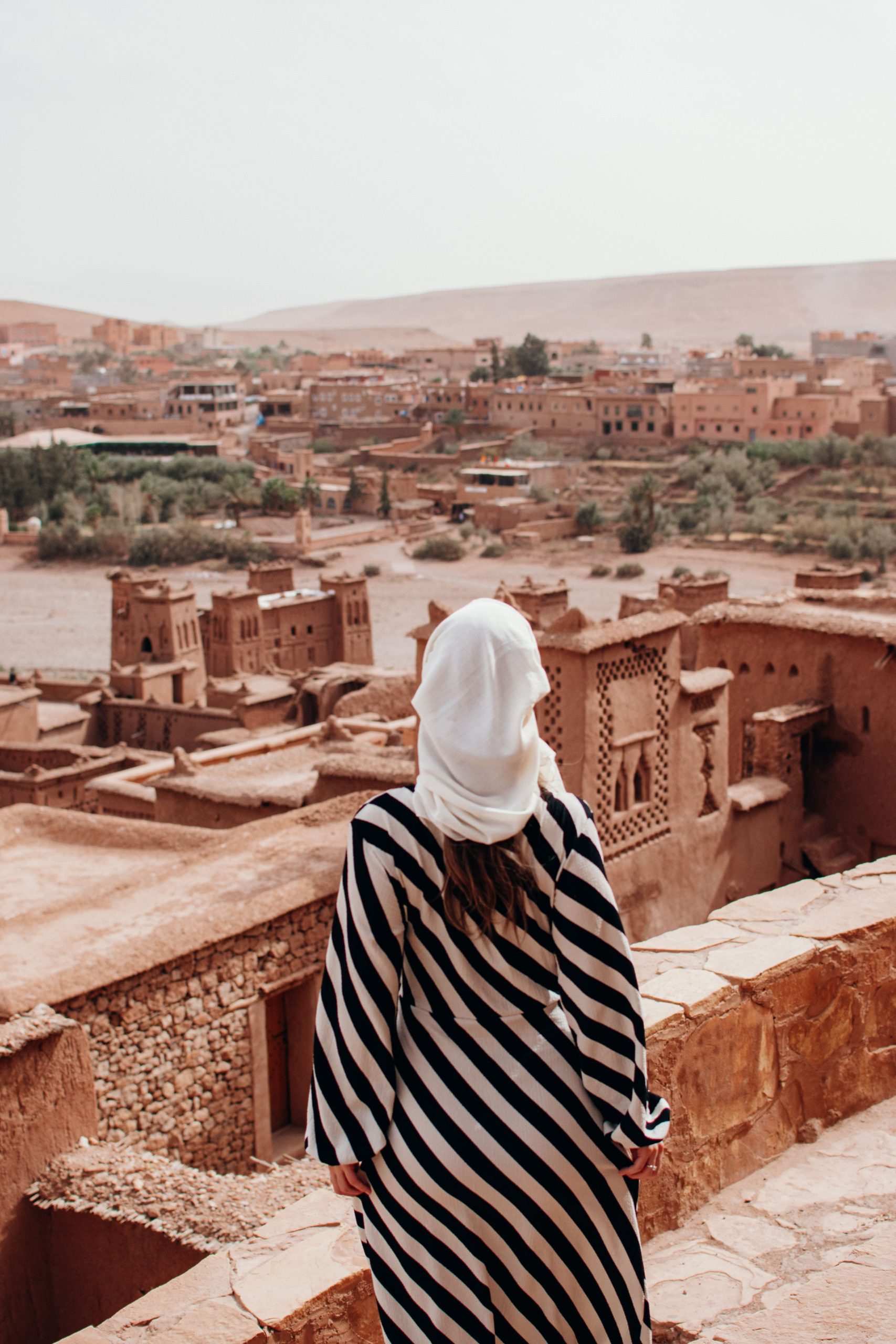 Woman in a striped dress and headscarf admiring At Benhaddous desert architecture